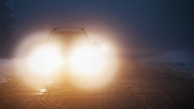 Oncoming car headlights flaring into a bright starburst on a dark road, the kind of glare cataracts cause at night
